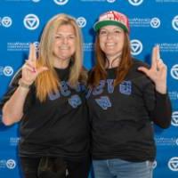 Two alums posing together by the backdrop.